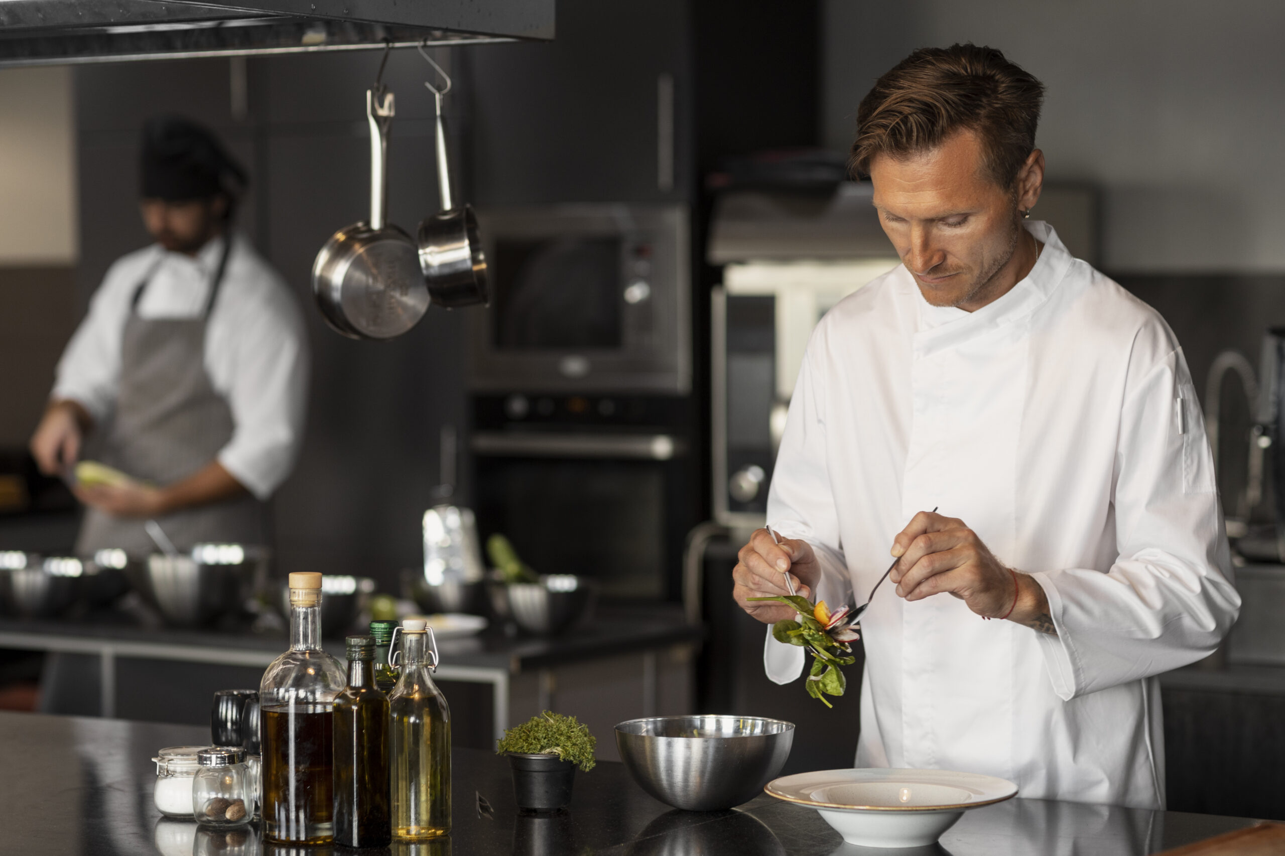 Cozinheiro está preparando um prato dentro de uma cozinha de restaurante, junto com outro cozinheiro em segundo plano