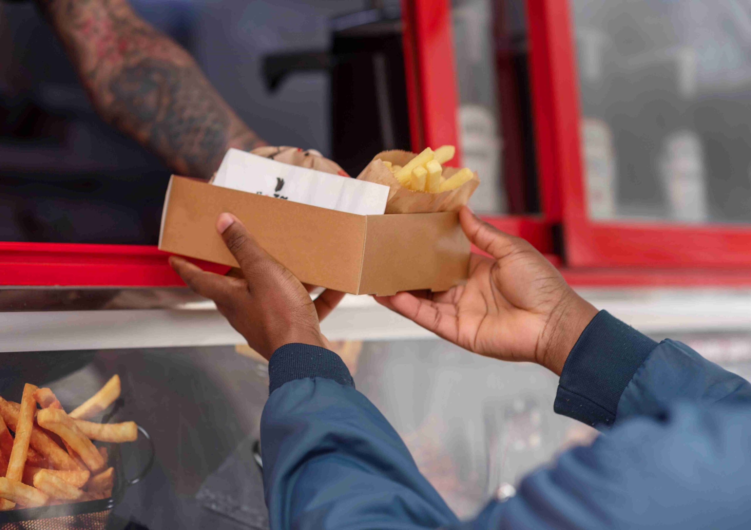 Pessoa segurando uma caixa com lanche e batata frita